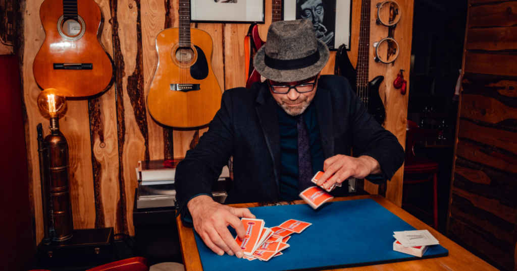 Stéphane Le Magicien, chapeau et lunettes, réalise un tour de cartes close-up sur un tapis bleu